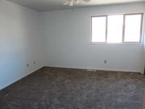 Unfurnished room featuring dark colored carpet and a ceiling fan