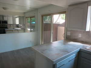 Kitchen featuring decorative backsplash, appliances with stainless steel finishes, a peninsula, dark wood-style floors, and white cabinets