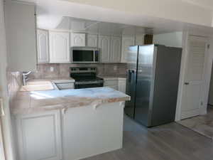Kitchen with a peninsula, white cabinets, appliances with stainless steel finishes, tile counters, and tasteful backsplash