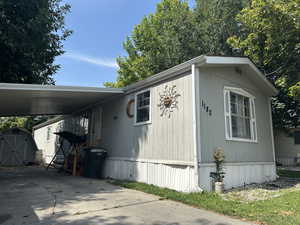 View of side of home with a storage unit, a carport, and concrete driveway