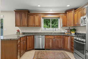 Kitchen with stainless steel appliances, brown cabinets, dark stone countertops, recessed lighting, and a peninsula