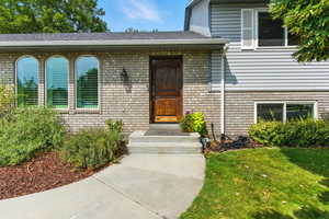 View of exterior entry with brick siding, a lawn, and roof with shingles