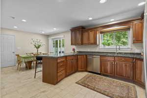 Kitchen with a peninsula, brown cabinets, recessed lighting, stainless steel dishwasher, and a kitchen bar