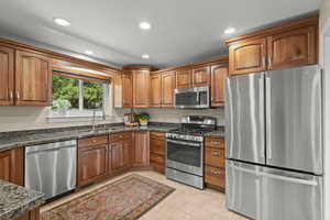Kitchen featuring stainless steel appliances, recessed lighting, brown cabinets, light tile patterned floors, and dark stone countertops