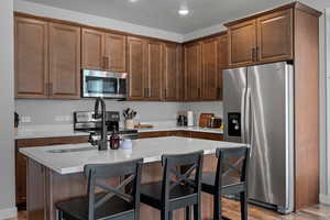 Kitchen featuring appliances with stainless steel finishes, a kitchen bar, a center island, dark wood-style flooring, and recessed lighting