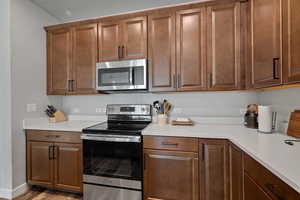 Kitchen with appliances with stainless steel finishes, wood finished floors, and brown cabinets
