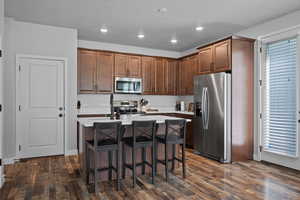 Kitchen with stainless steel appliances, a breakfast bar area, a center island, dark wood-style flooring, and recessed lighting