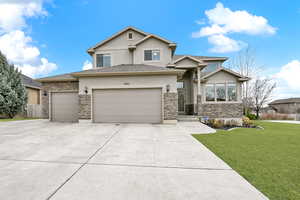 View of front of home with stucco siding, stone siding, driveway, an attached garage, and a front yard