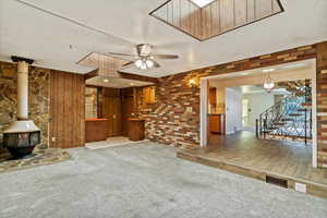 Unfurnished living room with a ceiling fan, carpet floors, a wood stove, a textured ceiling, and stairway