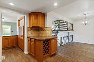 Kitchen featuring brown cabinetry, backsplash, dark stone countertops, a chandelier, and dark wood-type flooring