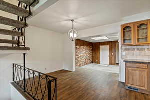 Unfurnished dining area with dark wood-style floors, wood walls, stairway, and a chandelier