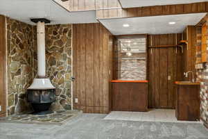 Kitchen featuring carpet, a wood stove, a textured ceiling, wooden walls, and tile patterned floors