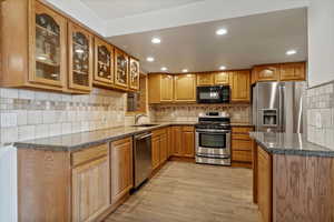 Kitchen with dark stone counters, appliances with stainless steel finishes, backsplash, glass insert cabinets, and recessed lighting