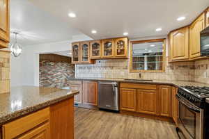 Kitchen featuring dark stone countertops, glass insert cabinets, appliances with stainless steel finishes, light wood-type flooring, and recessed lighting