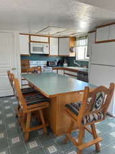 Kitchen featuring dark floors, brown cabinetry, white appliances, a breakfast bar area, and a textured ceiling