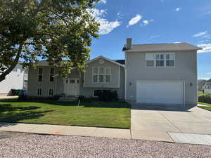 View of front of property featuring a chimney, a garage, concrete driveway, and a front lawn