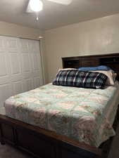 Bedroom with a closet, dark colored carpet, a ceiling fan, and a textured ceiling
