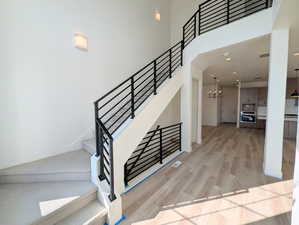 Staircase featuring a towering ceiling, metal railing, wood finished floors, and recessed lighting