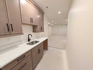 Wet bar in basement featuring concrete flooring, recessed lighting, and light stone counters