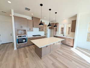 Kitchen with hanging light fixtures, open shelves, stainless steel appliances, a kitchen island, and light wood-type flooring