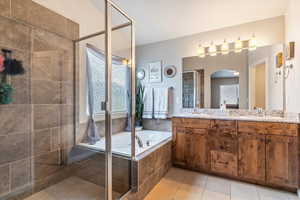 Full bathroom featuring a stall shower, a garden tub, double vanity, and light tile patterned floors
