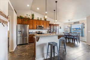 Kitchen with brown cabinets, stainless steel appliances, light stone counters, a breakfast bar, and decorative light fixtures