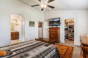 Bedroom with a spacious closet, vaulted ceiling, arched walkways, a ceiling fan, and light carpet