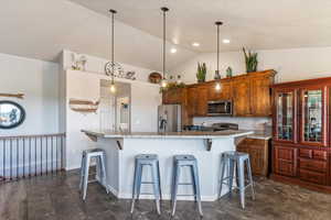 Kitchen with a breakfast bar, brown cabinets, hanging light fixtures, appliances with stainless steel finishes, and high vaulted ceiling