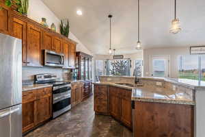 Kitchen with appliances with stainless steel finishes, hanging light fixtures, plenty of natural light, brown cabinetry, and lofted ceiling