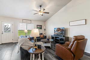 Living area featuring lofted ceiling, a ceiling fan, and dark wood-style flooring