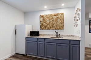 Kitchen featuring light stone counters, dark wood-style floors, black microwave, freestanding refrigerator, and recessed lighting