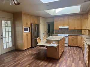 Kitchen featuring a kitchen breakfast bar, white appliances, a skylight, dark wood-style floors, and a center island