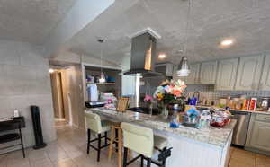 Kitchen featuring light tile patterned flooring, a breakfast bar area, island exhaust hood, pendant lighting, and tile walls