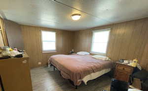 Bedroom with wood finished floors, a textured ceiling, and wooden walls