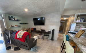 Living area featuring a textured ceiling, light tile patterned flooring, and tile walls