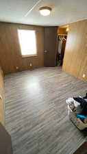 Unfurnished bedroom featuring wood walls, wood finished floors, a closet, and a textured ceiling