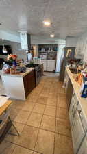 Kitchen featuring island range hood, a textured ceiling, washer and clothes dryer, appliances with stainless steel finishes, and light tile patterned floors