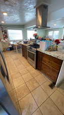Kitchen featuring island range hood, stainless steel range with gas cooktop, light tile patterned floors, light stone countertops, and a textured ceiling