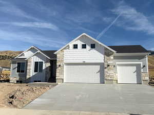 View of front of property with stone siding, driveway, an attached garage, board and batten siding, and roof with shingles