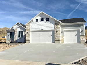 View of front of house featuring stone siding, concrete driveway, an attached garage, and board and batten siding
