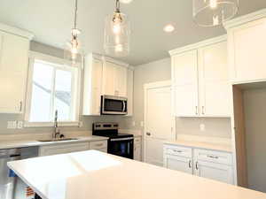 Kitchen with appliances with stainless steel finishes, pendant lighting, white cabinetry, recessed lighting, and light stone countertops