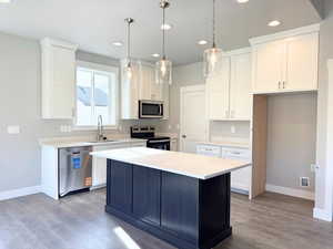 Kitchen with appliances with stainless steel finishes, hanging light fixtures, white cabinetry, a kitchen island, and recessed lighting