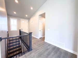 Hall featuring an upstairs landing, lofted ceiling, wood finished floors, and recessed lighting