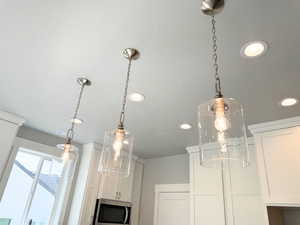 Kitchen view of pendant lighting, stainless steel microwave, recessed lighting, and white cabinetry