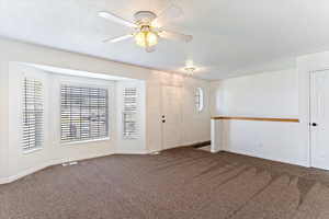 Spare room with dark carpet, a textured ceiling, and a ceiling fan