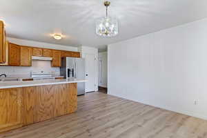 Kitchen featuring light countertops, light wood-style floors, brown cabinetry, a peninsula, and decorative light fixtures
