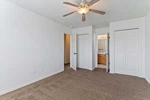 Unfurnished bedroom with multiple closets, carpet flooring, ensuite bathroom, and a ceiling fan