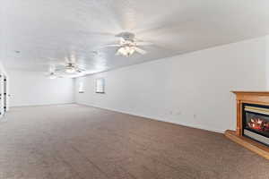 Unfurnished living room with a glass covered fireplace, a textured ceiling, carpet, and a ceiling fan
