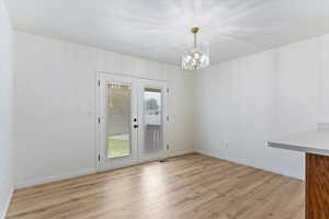 Unfurnished dining area featuring light wood-style floors, french doors, and a chandelier