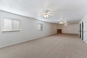 Spare room with light colored carpet, a lit fireplace, a textured ceiling, and ceiling fan